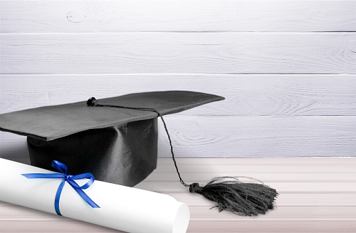 Graduation hat with book and diploma on wooden desk