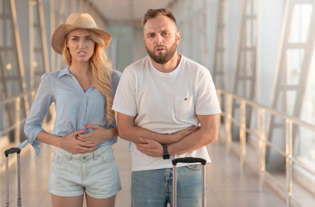 couple suffering from stomachache, arriving at airport - stomachache illness pain indigestion imagens e fotografias de stock