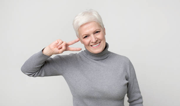 istock Aged lady showing v-sign peace gesture, smiling at camera 1168003440