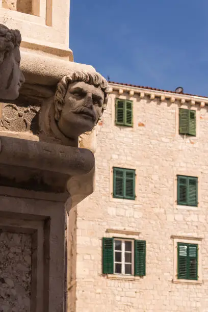 Building made of stone. Walls outdoors  decored with the sculptures of human heads (unknown models). House and a blue sky in the background. St. James Cathedral, Sibenik, Croatia.