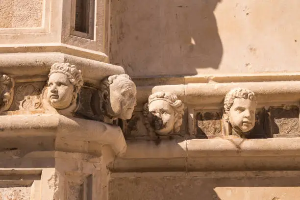 Building made of stone. Walls outdoors enlighted by sunlight, decored with the sculptures of human heads (unknown models). St. James Cathedral, Sibenik, Croatia.