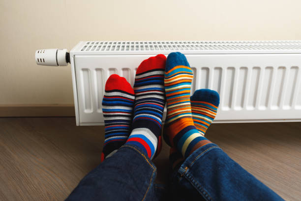 gambe con calzini colorati di fronte al radiatore di riscaldamento - couple abstract multi colored new foto e immagini stock