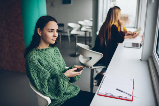istock Young caucasian woman using mobile phone and wireless connection sitting in loft interior coworking space, thoughtful creative female blogger concentrated on idea for publication holding smartphone 1168010606