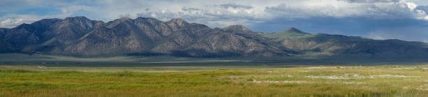 istock Panoramic view of green arid wetland with mountain range on the background during clouded summer 1168017483