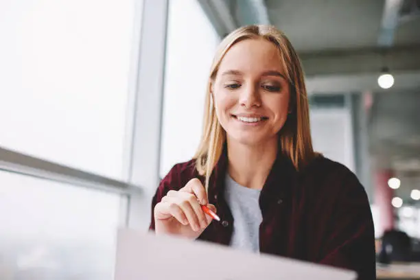 Photo of Positive blonde woman fill in information in questionnaire making application for hire on vacancy, smiling female students satisfied with know answers for test completing writing with pen indoors