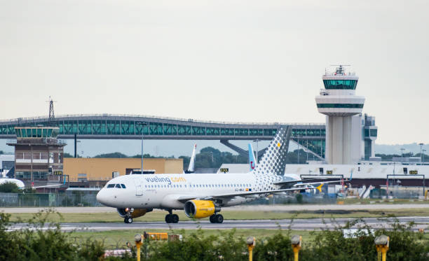 un airbus a319-100 di vueling airlines s.a. spegne la pista di fronte alla torre di controllo del traffico aereo e al ponte gatwick pier 6 - air traffic control tower foto e immagini stock