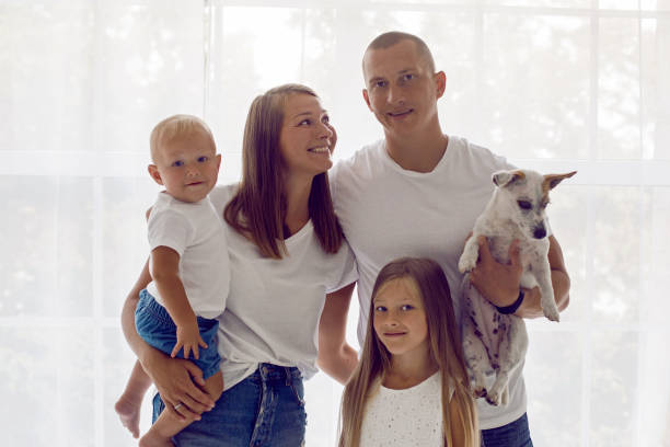 familia de cuatro y un perro de pie por una gran ventana - dog baby t shirt child fotografías e imágenes de stock