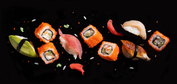 piezas de sushi entre palillos, volando separados sobre fondo negro. - sushi restaurant fish japanese culture fotografías e imágenes de stock