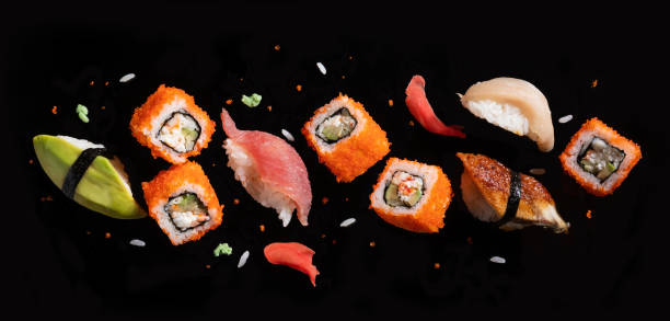 Sushi pieces between chopsticks, flying separated on black background.