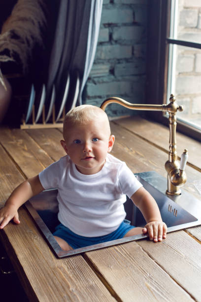 niño en una camiseta blanca sentado en el fregadero de la cocina - dog baby t shirt child fotografías e imágenes de stock