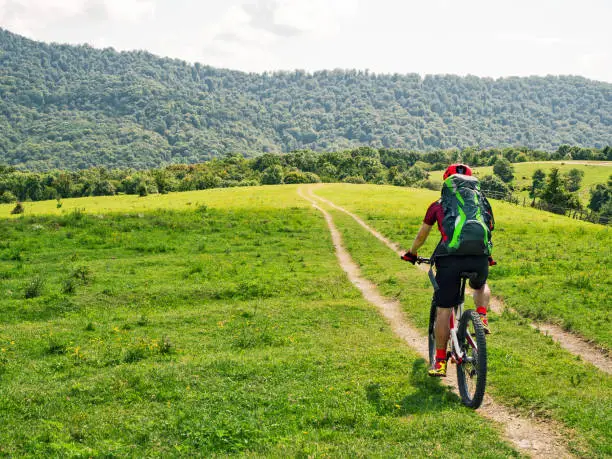 Photo of Bicyclist with backpack riding mountain bike on meadow path