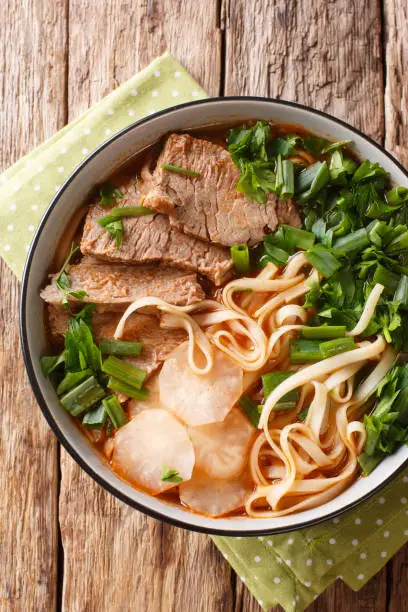 Lanzhou beef noodles recipe the beef broth served with melt-in-your-mouth beef slices, tender radish, chili oil and noodles closeup in a bowl on the table. Vertical top view from above