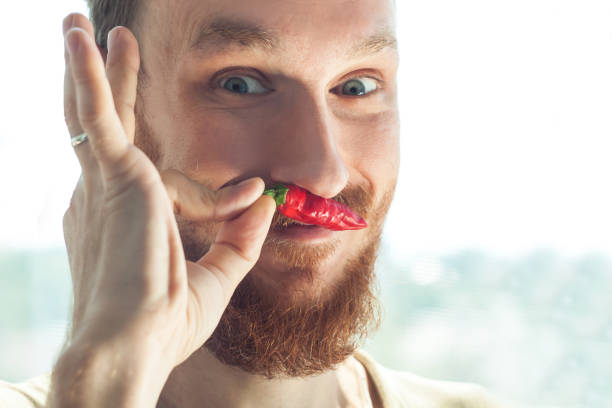 Handsome bearded man bites a red hot chili pepper and smiles.