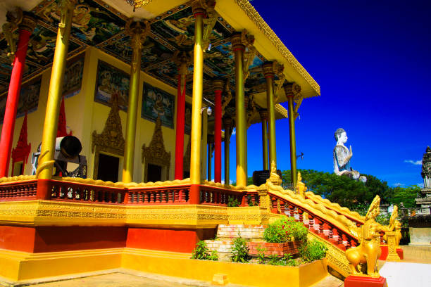 View on golden pillars, drum and white buddha statue against blue sky at Buddhist temple - Wat Ek Phnom, near Battambang, Cambodia