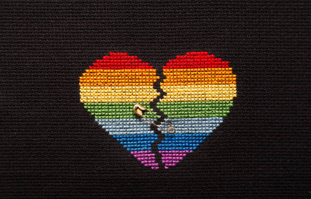 istock Broken heart embroidered on black cloth with rainbow threads. The heart is joined by a pin. 1168039270