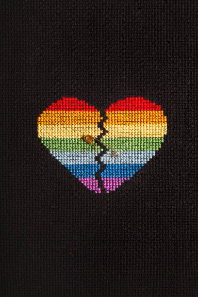 istock Broken heart embroidered on black cloth with rainbow threads. The heart is joined by a pin. 1168039272