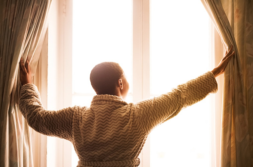Rear view shot of a young woman opening the curtains in the morning to get fresh air
