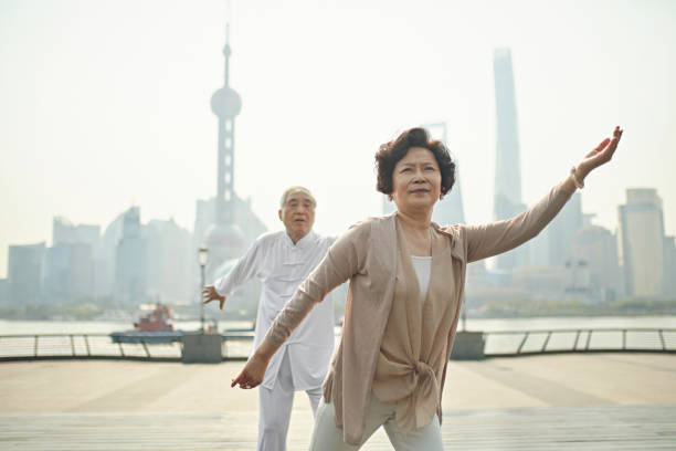 Senior Chinese Couple in Tai Chi Pose on Waitan Waterfront Close-up of senior Chinese woman and male companion doing tai chi on The Bund with Pudong cityscape in background. view into land stock pictures, royalty-free photos & images