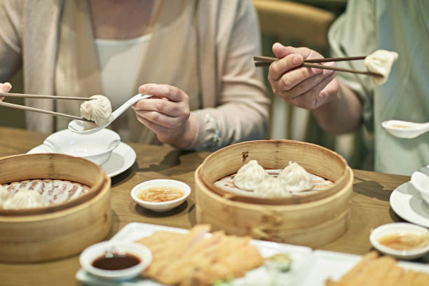 Close-up of Chinese restaurant goers eating dumplings presented in bamboo steamers with dipping sauces.