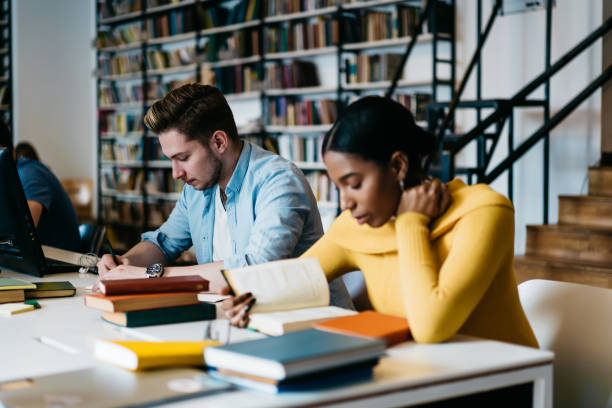 istock Concentrated multicultural students preparing for upcoming exams reading textbooks in library.Caucasian hipster guy writing homework test while dark skinned colleague searching information in book 1168051975