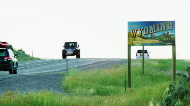 Vehicles Drive by the Wyoming State Line Sign on the Wyoming/Colorado Border at Sunset