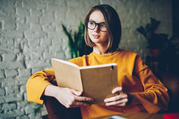 istock Thoughtful clever student in stylish optical eyeglasses thinking on interesting plot of book written by famous novelist.Pondering young woman with short haircut looking away during reading bestseller 1168055062