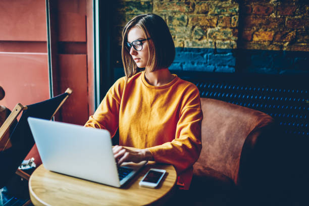 istock Smart concentrated female copywriter in eyeglasses working freelance at laptop device connected to high speed 4G internet in coffee shop.CLever female designer developing new graphic at netbook 1168055105