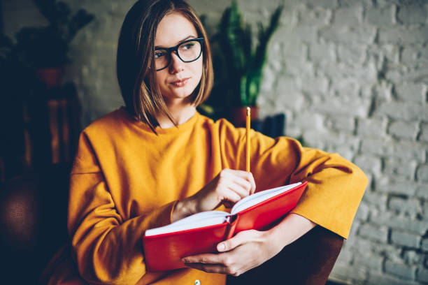 istock Pondering female reader thinking on continuing love story from literature book enjoying recreation time in stylish coworking space.Dreamy hipster girl studying remotely in coffee shop interior 1168055133