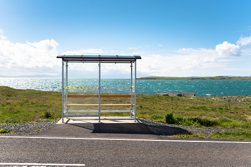 Deserted glass shelter at a bus stop on a coastal road on a clear summer day. Orkney Islands, Scotland, UK.
