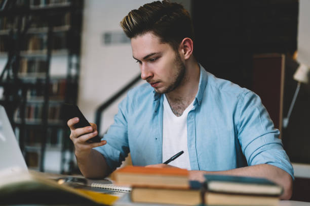 istock Pensive young hipster guy making money transaction via app on smartphone while sitting in campus,millennial male using mobile phone checking new feeds in social networks via wireless internet 1168056801
