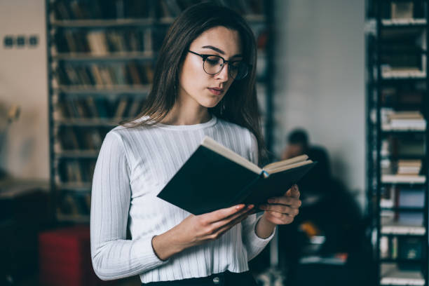 istock Serious young woman in spectacles concentrated on reading interesting book choosing literature in store,clever female student holding textbook analyzing information for learning to exams in college 1168056839