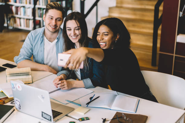 istock Young multiracial group of students making funny faces for common picture made on fron camera of smartphone, happy teen hipsters friends taking selfie during learning in college library together 1168056854
