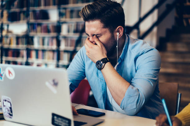 istock Frustrated caucasian student depressed from overworking at modern laptop device connected to wireless internet sitting in library.Stressed hipster guy has headache while listening audio in earphones 1168056927