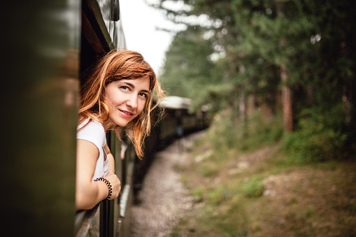 Happy smiling redhead woman looks out from window traveling by train