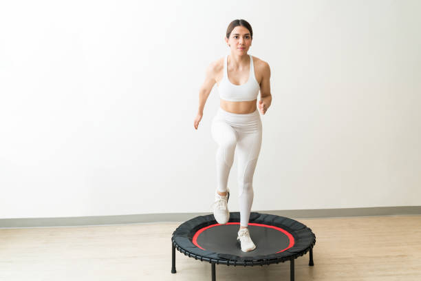 Dedicated young woman in white sportswear trampolining against wall during high intensity interval training