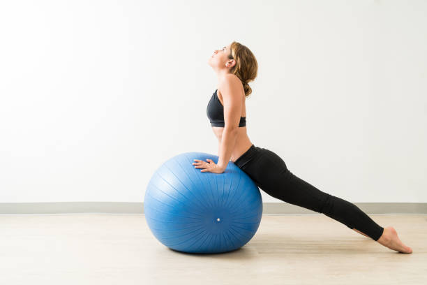 Side View Of Young Woman Stretching During Workout Pretty brunette female exercising while leaning on fitness ball at training studio fitness ball photos stock pictures, royalty-free photos & images