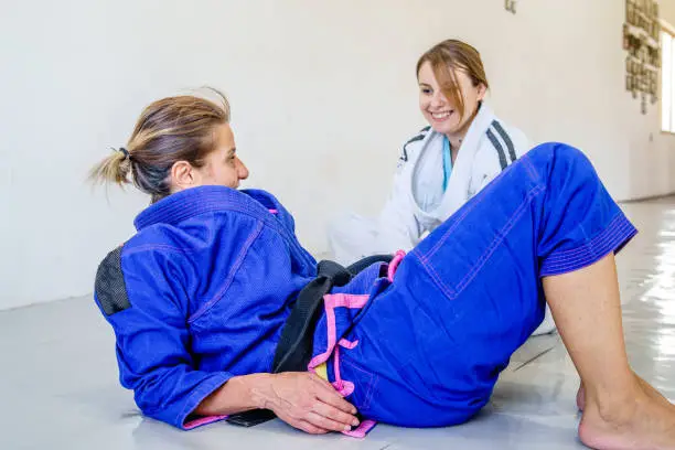 Two brazilian jiu jitsu bjj judo female judoka fighters women sitting and talking to each other during the brake in the training on the mats wearing kimono gi