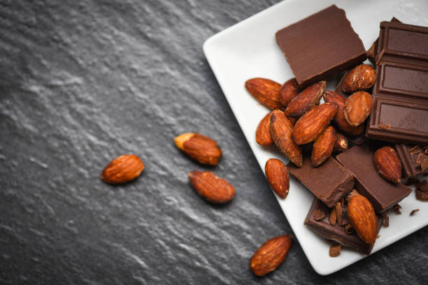 istock chocolate bar with almonds nut on white plate on the dark background - chunks candy sweet dessert and snack 1168073567
