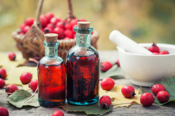 mortier de baies d'aubépine, deux bouteilles de teinture ou d'infusion et panier de pommes d'épine sur planche en bois. phytothérapie. - haw photos et images de collection