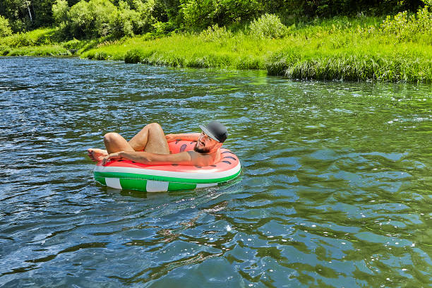 o homem no anel inflável está flutuando abaixo do rio. - inner tube swimming lake water - fotografias e filmes do acervo