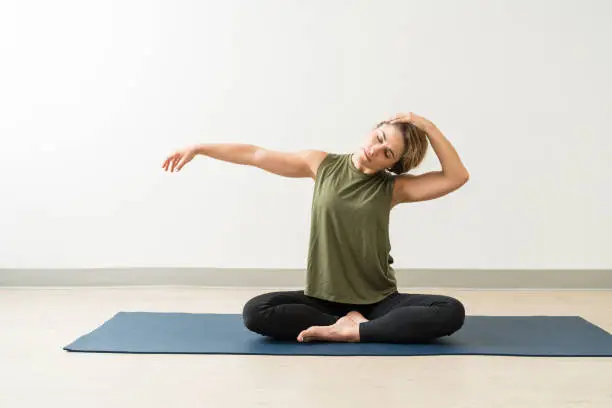 Young brunette female stretching neck while practicing yoga during workout