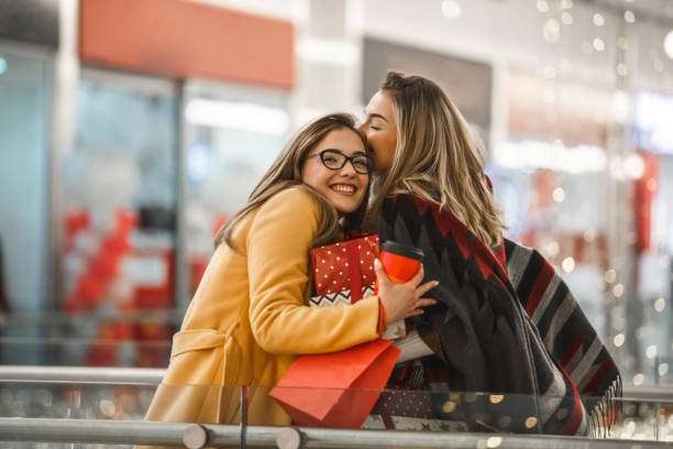 Sisters sharing Christmas presents Beautiful young women are hugging and sharing presents after shopping. happy sibling day stock pictures, royalty-free photos & images