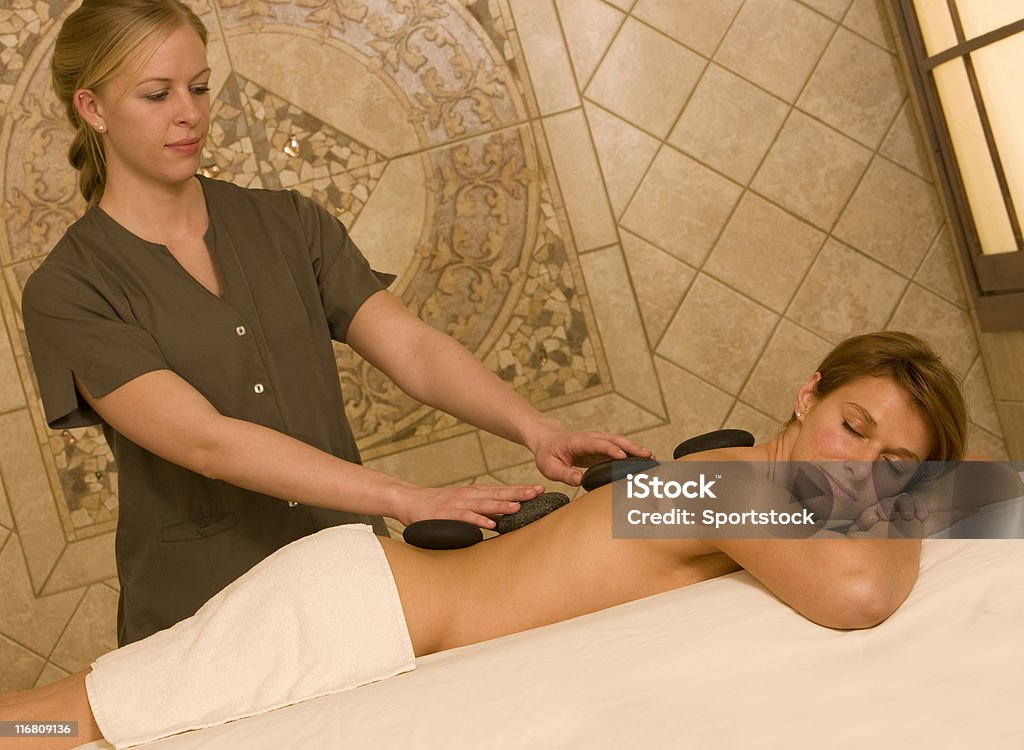 Pretty Woman Getting A Massage A beautiful young woman getting a hot stone massage in a treatment room at a health spa. Adult Stock Photo