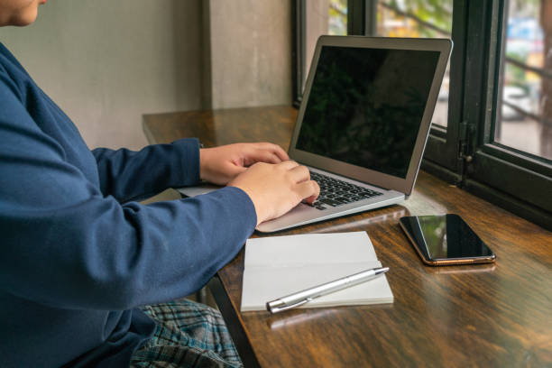 istock Asian woman typing laptop on rustic table next to window 1168095783