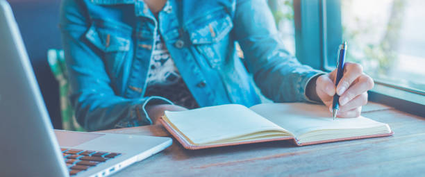 istock Woman hand is writing on notebook with a pen in the office.Web banner. 1168099223