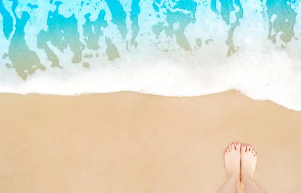 Photo of Feet on beach background. Top view on naked feet and legs in sand with wave motion coming to the foot - foaming sea texture. Summer and vacation holiday concept.