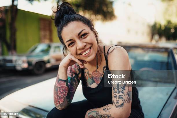 Tattooed Latina Smiling Outdoors And Sitting On Car Hood Stock Photo - Download Image Now