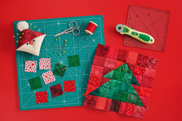 christmas tree patchwork block, craft mat, bright square pieces of fabric, pincushion like santa and quilting accessories on red background - christmas quilt craft patchwork imagens e fotografias de stock