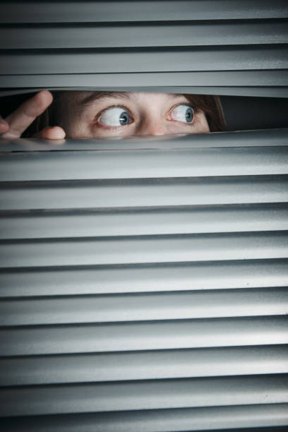 istock Terrified young woman peeps through blinds 1168124900
