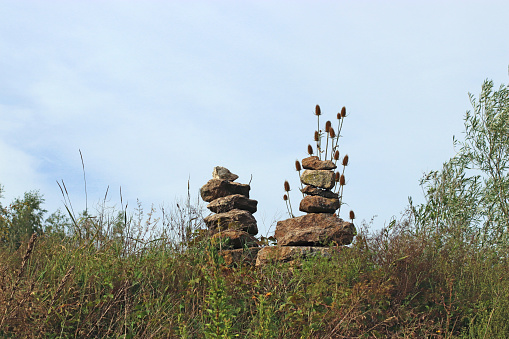 two cairns standing in a meadow on a hill in front of blue sky